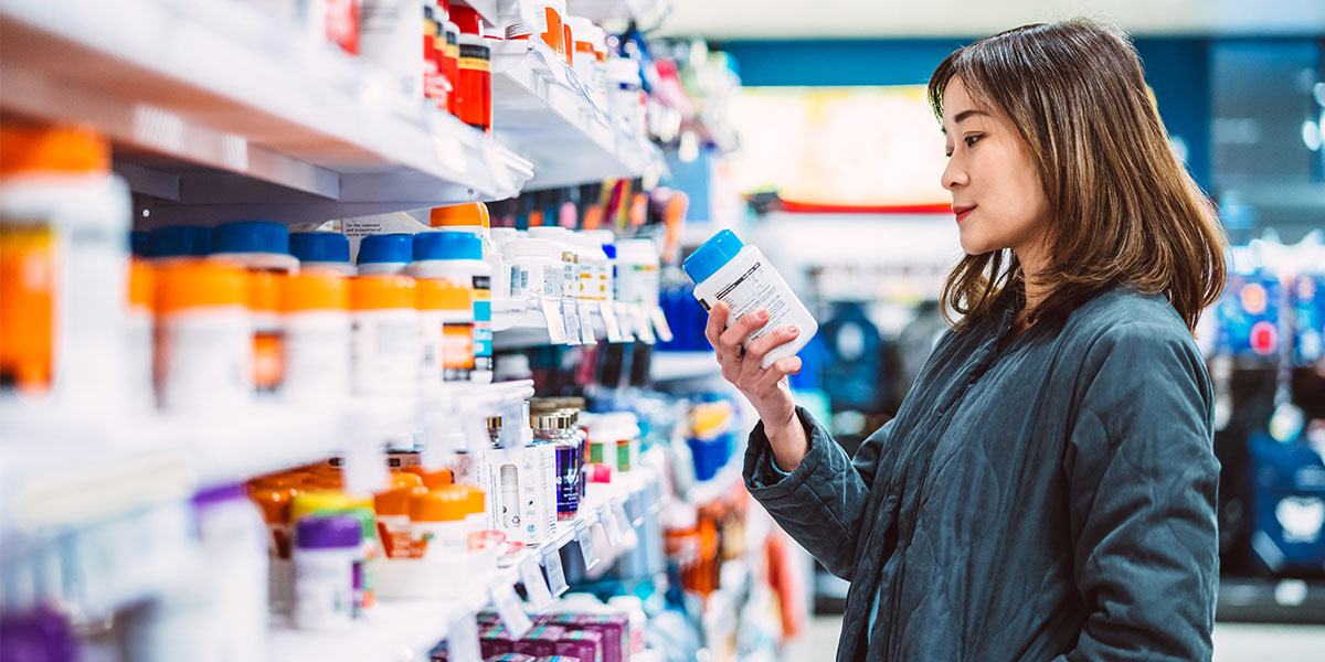 Woman reading the ingredient label while shopping for multi vitamin & health supplements on shelf in supermarket.