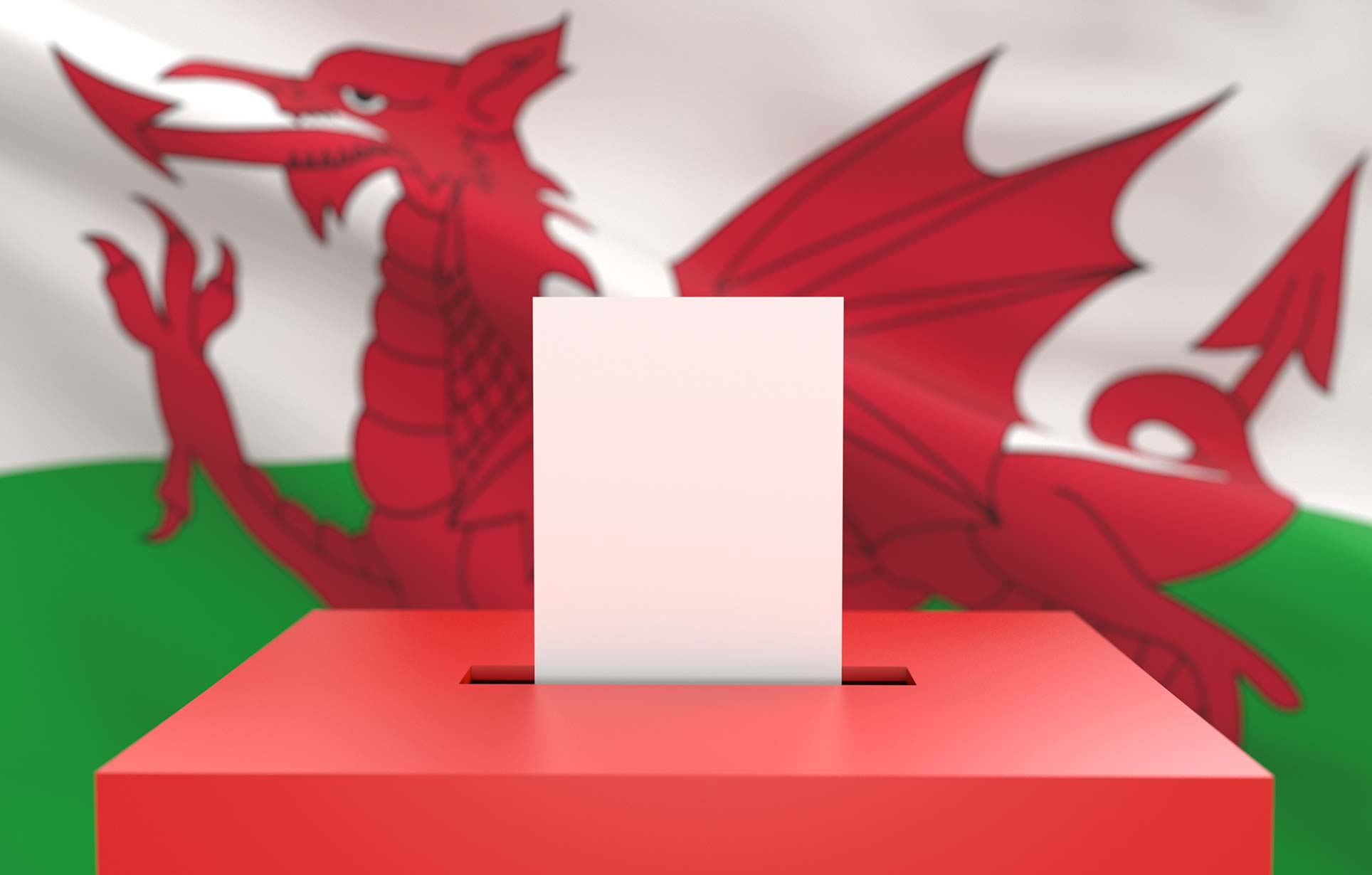 A ballot box with a voting paper being inserted, in front of the Welsh flag featuring a red dragon on a white and green background.