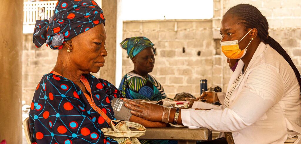 A healthcare worker checks blood pressure of an elderly woman in a rural clinic setting.